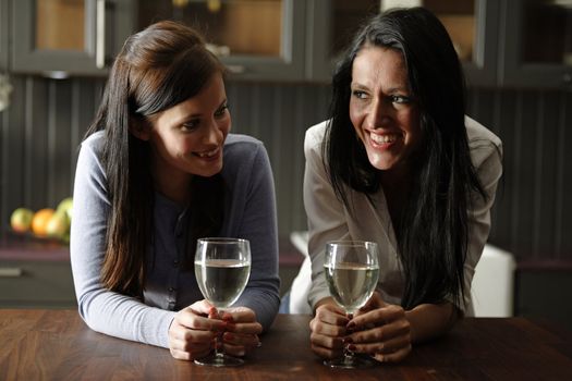 Two attractive young friends laughing and drinking wine in their kitchen.