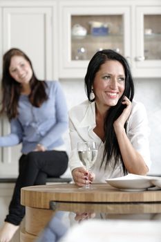 Two attractive young friends laughing and drinking wine in their kitchen.