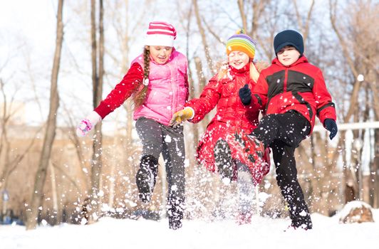 Boy and girls playing with snow in winter park, spending time together outdoors