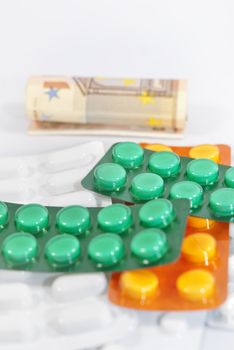 Pills and money (euros banknotes) on white background