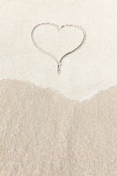 handwritten heart on sand with wave approaching 