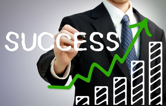 Businessman drawing a rising arrow over a growing bar graph showing success