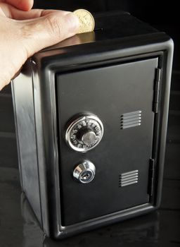 Male hand putting money in a black strongbox over black background