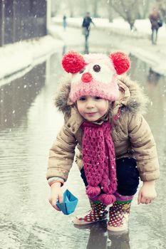 little girl plays with paper ships in a spring puddle