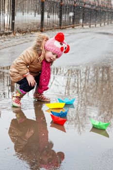 little girl plays with paper ships in a spring puddle