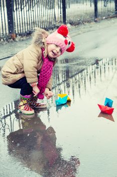 little girl plays with paper ships in a spring puddle