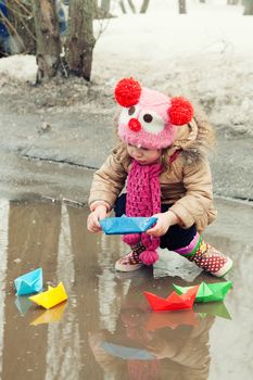 little girl plays with paper ships in a spring puddle