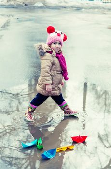 little girl plays with paper ships in a spring puddle