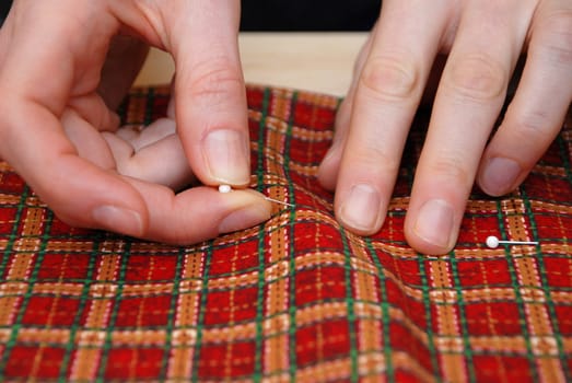 Closeup of two hands sticking pins into festive red plaid fabric