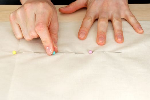 Closeup of a woman's hands pinning large upholstery pins into plain fabric