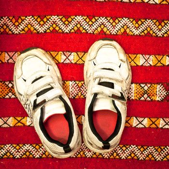 Pair of worn white kids trainers on a red rug