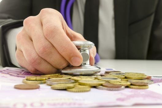 Detail of business man holding stethoscope over European currency.