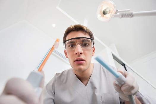 Serious young male holding dental tools with man in the background
