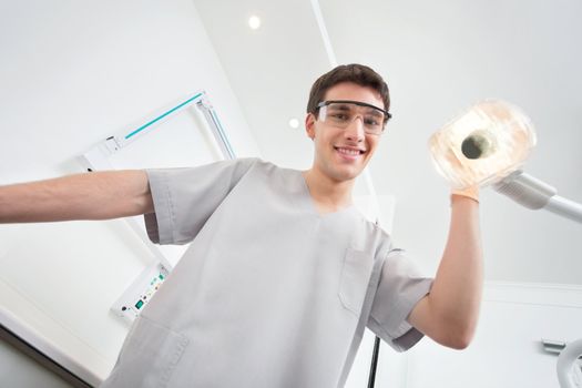 Young male dental assistant smiling and adjusting the lamp