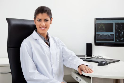 Portrait of pretty female dentist sitting at her desk with teeth x-ray on screen