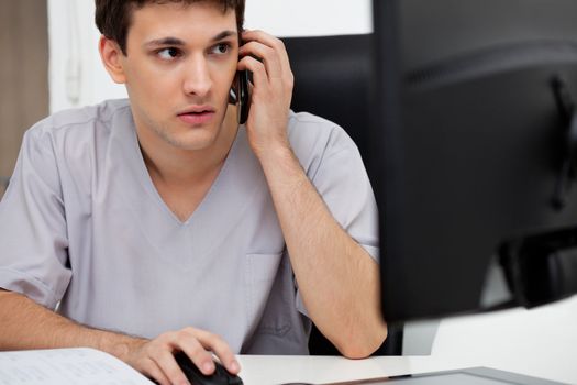 Doctor working on computer while talking on cell phone