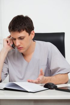Serious male doctor talking on mobile phone at his desk