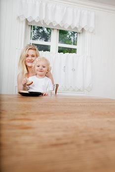 Smiling baby boy eating bread while sitting on lap of mother