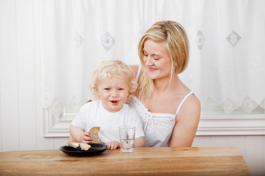 Happy beautiful mother with blond little boy eating bread