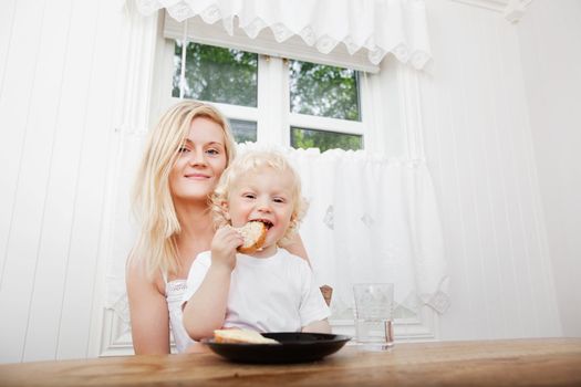 Portrait of cute little boy eating bread with mother at home