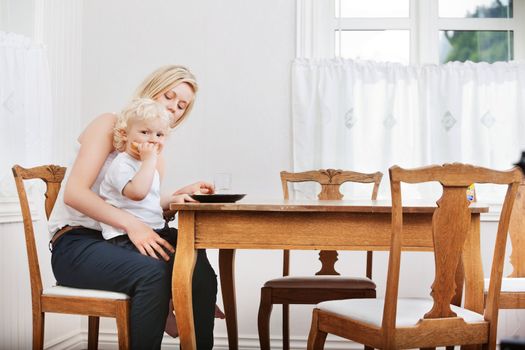 Portrait of baby boy eating bread while sitting on mother's lap at dining table