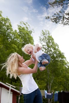 A young mother playing with excited toddler son, throwing him in the air.