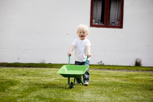 A young child pushing a wheelbarrow outdoors in a rural farm setting