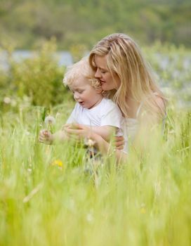 A mother and son making a wish on a dandelion in a green meadow