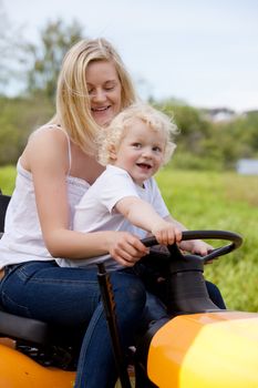 A mother driving a lawn mower tractor with happy smiling son