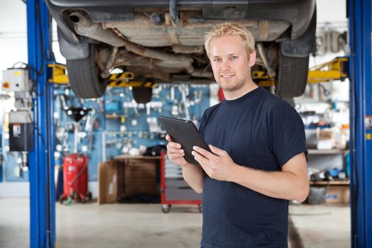 Portrait of young mechanic holding digital tablet in his auto repair shop