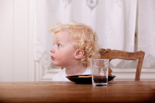 A curious young boy sitting at a meal table with bread on his plate