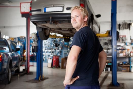 A happy smiling mechanic in an autio repair shop, looking at the camera