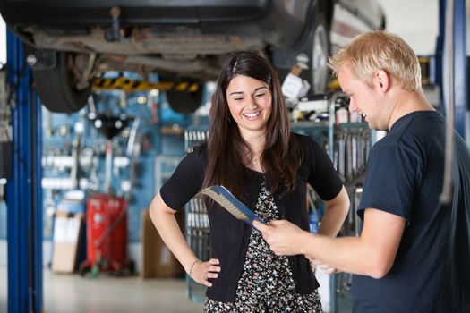 Young mechanic and woman looking at notepad and smiling in garage