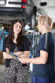 Smiling young woman and mechanic talking to each other in auto repair shop