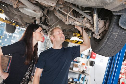 Young mechanic and woman looking at machine of car in auto repair shop