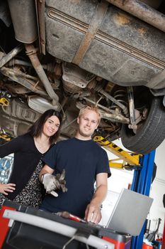 Portrait of young female standing with mechanic using laptop in auto repair shop