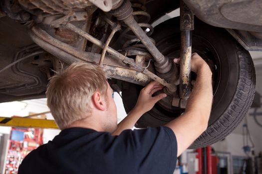 A male mechanic inspecting a CV joint on a car in an auto repair shop