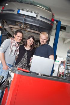 Smiling young couple standing with mechanic using laptop in auto repair shop