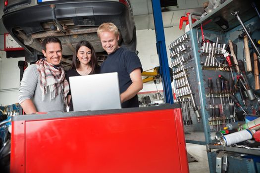 Young smiling couple standing with mechanic using laptop in auto repair shop