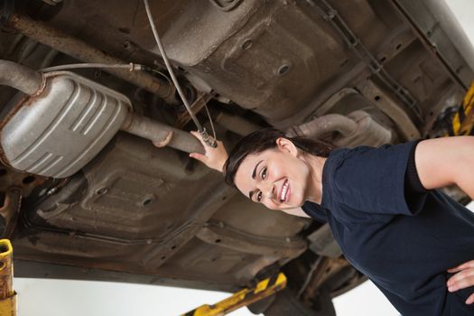 Low angle view of smiling young female mechanic repairing car in auto repair shop