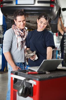 Female worker using laptop while standing next to client in garage with person in the background