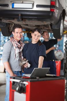 Portrait of female worker using laptop while standing next to the client in garage with person in the background