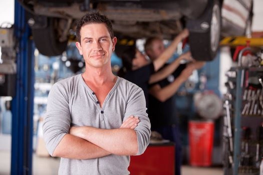 Portrait of a male mechanic looking at the camera with workers in the background