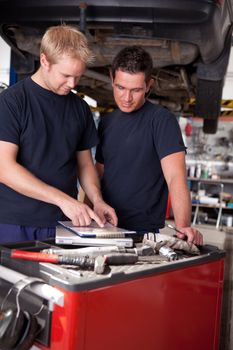 A pair of mechanics working on a car looking a service order
