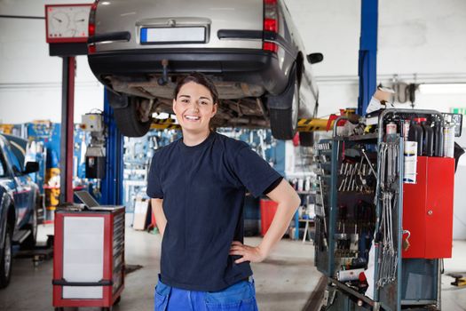 Portrait of smiling young female mechanic with hands on hips in auto repair shop