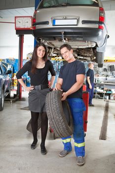 Full length portrait of female customer and mechanic holding tire in hand