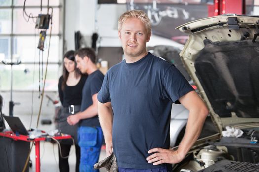 Portrait of a  young mechanic in auto repair shop with customer in background