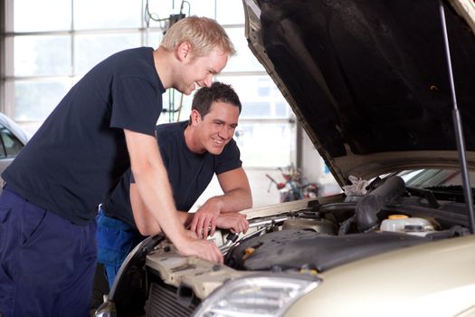 Two man mechanics smiling and working under the hood of a car, shallow depth of field, sharp focus on rear mechanic