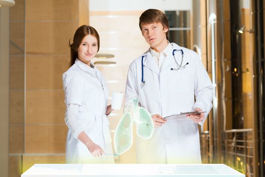 two doctors stand near glowing table discussing. projected objects on a desk