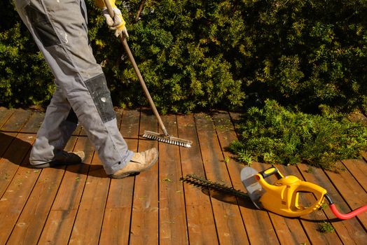 A person is sweeping the terrace after pruning the hedge